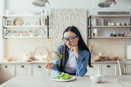 对厨房饮食不满意的亚洲年轻女性 吃健康食品的女性 尝试吃沙拉和健康食品的女性 在家的青少年图片