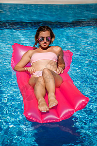 穿着粉红色比基尼泳衣的女人漂浮在可充气的粉色床垫上 Spf和防晒霜是被涂过的太阳镜火烈鸟游泳衣闲暇游泳温泉横幅娱乐身体泳装图片