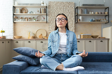 美丽的亚洲女人坐在沙发上在家休息 穿着莲花装坐沙发和冥想 在客厅做呼吸锻炼图片