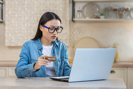 沮丧和悲伤的抑郁症女性试图在网上商店进行在线购买 亚洲女性坐在家里的厨房里使用笔记本电脑和银行信用卡 无法在线支付预算商务信用客图片