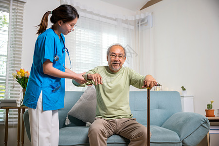 年轻妇女帮助支持矫形病人在家用步行拐杖起身 协助其康复看门人沙发保健卫生老年男性成人照顾者护理女士图片