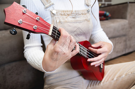 特写 尤克里里在女性手中 嬉皮士在家学习弹奏乐器 坐在沙发附近的地板上图片