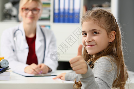 美丽的小女孩露出大拇指 医生坐在背景中坐着图片