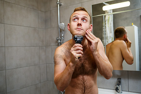 一名男子在镜子前用电剃刀刮脸部 皮肤刺激 浴室程序等脸颊胡须男性成人房子男人剃须刀头发剃刀刮胡子图片