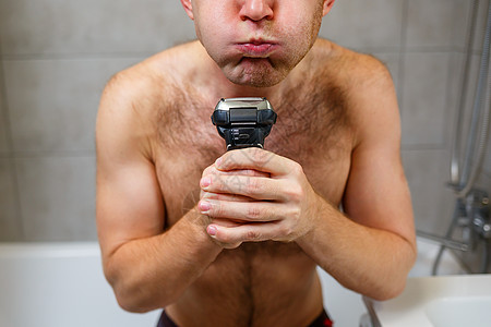 一名男子在镜子前用电剃刀刮脸部 皮肤刺激 浴室程序等剃刀大男子男性头发生活成人脸颊理发师护理主义图片