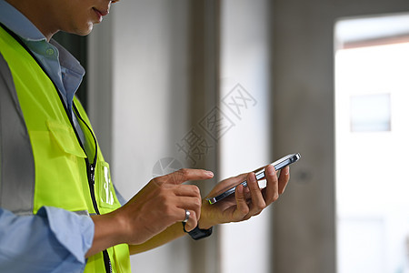 智能工地身穿反射夹克的工程师男子在建筑工地站立并使用智能电话被裁剪背景