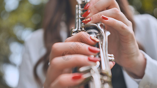 一个女孩夏天在公园里弹单簧管 手贴紧一点 举起手来旋律成人演奏家按钮演员艺术女性娱乐学校交响乐图片