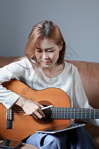 在沙发上弹吉他 度假时放松压力的年轻亚洲女人的肖像家庭生活摄影青少年活动休闲社交学习成人指板客厅图片