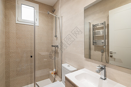 明亮的米色浴室配有光滑的瓷砖墙壁和照明 浴室配有带玻璃栏杆的淋浴 带水槽的大镜子 用于晾干毛巾的散热器图片