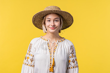 在黄色工作室背景上穿传统刺绣衣的乌克兰金发年轻女子的肖像 自信的阳光服装 稻草帽图片