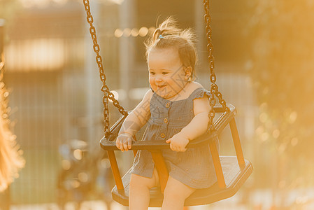 一个快乐的幼儿女婴 穿着洋装 在暖暑夜秋千婴儿童年幸福微笑公园喜悦孩子女孩情感惊愕图片