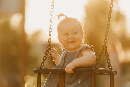 一个快乐的幼儿女婴 穿着洋装 在暖暑夜秋千情感婴儿幸福喜悦惊愕微笑孩子们女孩操场孩子图片