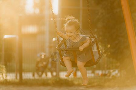 一个快乐的幼儿女婴 穿着洋装 在暖暑夜秋千童年女孩操场婴儿情感微笑孩子女性惊愕公园图片