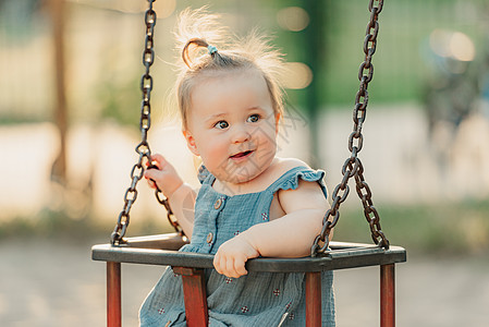 一个快乐的幼儿女婴 穿着洋装 在暖暑夜秋千喜悦微笑幸福孩子们婴儿童年操场惊愕情感公园图片