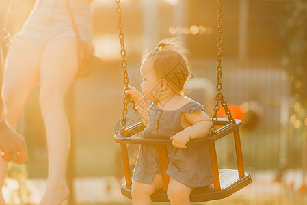 一个快乐的幼儿女婴 穿着洋装 在暖暑夜秋千孩子操场微笑女性情感婴儿幸福惊愕童年公园图片