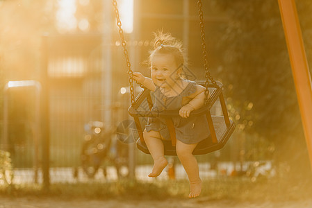 一个快乐的幼儿女婴 穿着洋装 在暖暑夜秋千女性喜悦女孩公园孩子童年情感孩子们惊愕微笑图片