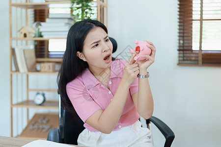 一位亚洲女商务人士在中小企业业务中表现出严肃而焦虑的表情 但粉红猪存钱罐里没有钱 储蓄计划购物技术营销计算经理银行业桌子成人平衡图片