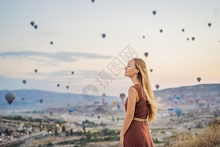 土耳其气球在土耳其卡帕多细亚看热气球的女游客 土耳其概念中的快乐旅行 山顶上的女人享受美妙的景色女孩蜜月石头旅游地质学阳光夫妻空气悬崖天空背景