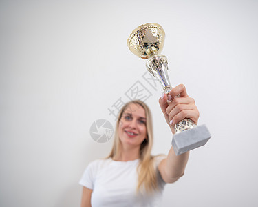 金发女人笑着拿着金杯 站在白色的墙壁上成功金发女郎快乐冠军女士成就推介会领导女孩锦标赛图片
