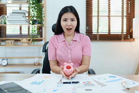 一位亚洲女商务人士在中小企业业务中表现出严肃而焦虑的表情 但粉红猪存钱罐里没有钱 储蓄计划计算器平衡桌子银行业金融报告企业家预算图片