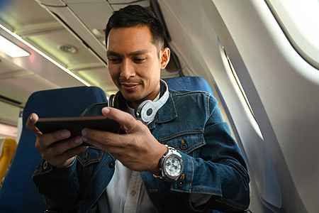 快乐的时髦男士旅行者在飞行期间通过智能手机观看电影或娱乐媒体图片
