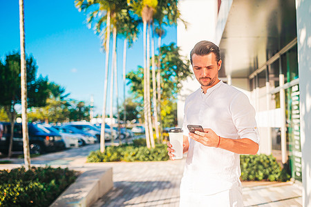 快乐的年轻caucasian男子与咖啡使用智能手机去户外图片