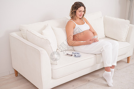 孕妇坐在白色沙发上 有智能手机 胎儿超声波检查腹部新生活肚子喜悦胚胎婴儿照片妇科享受家庭图片