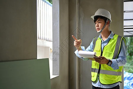 穿着安全头盔和防伪衣的青年男子检查员 手持剪贴板 检查重建后的建筑工作职场职业领班建筑师财产项目工地男人建筑工人图片