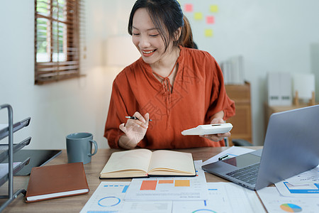 一位深思熟虑的亚洲女商务人士在她桌上使用一台计算机查看财务报表和制定营销计划时所描绘的一幅形象商务检查投资文书数字组织陈述控制平图片