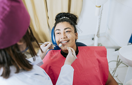 女牙医对微笑的病人进行牙科检查的特写 病人躺在椅子上对牙医微笑 牙医对女病人进行牙科检查图片