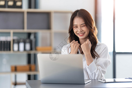 使用笔记本电脑的美丽的亚洲女性 令人振奋和以商业成功的好消息来庆祝 小生意启动概念 笑声企业家喜悦办公室乐趣成人优胜者学生胜利人背景图片