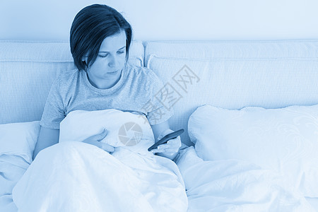 女人坐在床上时用智能手机 上面盖着哑巴说谎细胞互联网女士房子阅读黑发房间电话蓝色图片
