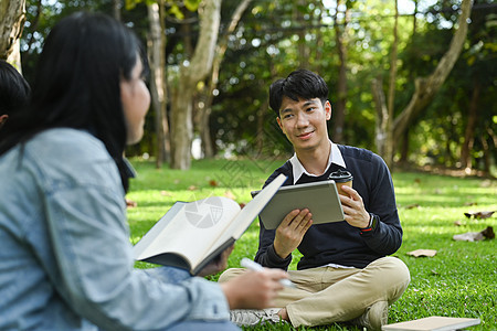 在数字平板电脑上检查大学进度表 坐在校园绿草地上与朋友交谈时微笑着年轻男子的笑容图片