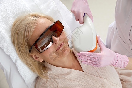 中年妇女在美容诊所接受激光治疗时佩戴保护眼镜的女中年人电解化妆师美容师女孩粉刺药品身体皮肤皮肤科医生图片
