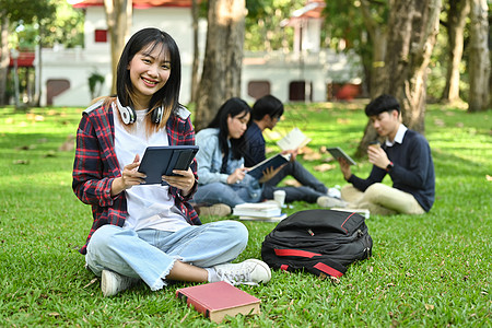 在校园绿草上使用数字平板电脑的亚洲女子学院或大学女生和大学生 令人欢欣鼓舞图片