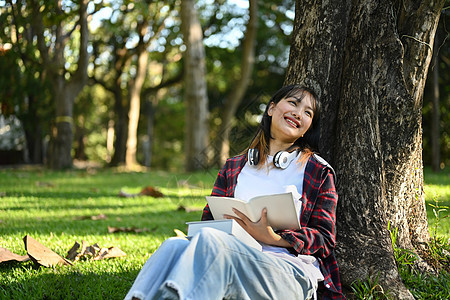 喜悦的年轻女子在阳光明媚的美丽日子里 在绿草上阅读树下读书图片