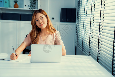 一位年轻的亚洲妇女坐在办公室的办公桌前电脑企业家经理商务成人写作女性技术套装员工图片