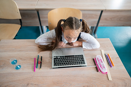白种女孩坐在学校的桌子上 用笔记本电脑学习 桌上有沙漏滴漏知识孩子教育学生小学生女学生时间技术时间表图片