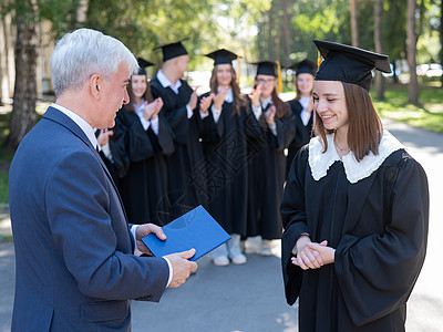 教师与学生握手 并在户外颁发文凭 一组大学毕业生 见AC 54970女孩成就帽子礼物教育文件夹认证学校混血儿裙子图片