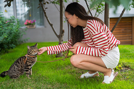 年轻女子在户外走着小猫咪猫咪皮带毛皮宠物小猫后院公园叶子动物冒险图片