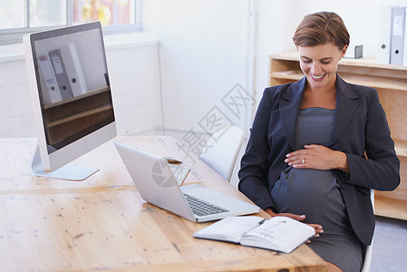 我迫不及待地想见你 一个怀孕的女商务人士坐在她的办公桌前 在她胃里满脸笑容图片