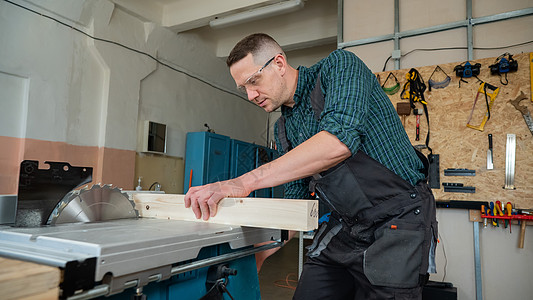 木匠在圆形机器上切开木板修理工技术员承包商工艺木工材料维修乐器围裙男性图片