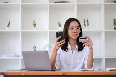 年轻的亚裔女性在支付方面遇到问题 悲伤的女性网络购物者坐在沙发上拿着电话和信用卡 感到沮丧 担心卡账户超支的痛苦女士账单商业借方图片