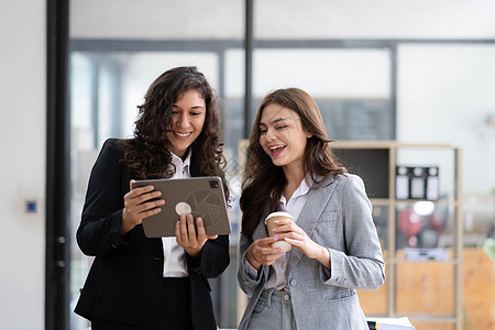 两名美丽的亚洲女商务人士利用数字平板电脑咨询和分析办公室工作的信息站立起来 她们站在办公室工作公司讨论战略技术企业家微笑会议职场图片