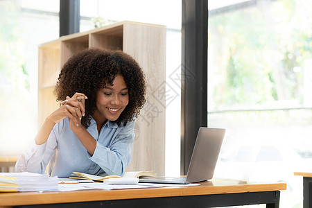 坐在家中办公室的办公桌前用笔记本电脑在线工作的年轻非洲女性创业者微笑着笑脸职场投资女士员工管理人员女孩互联网商业企业家成人图片