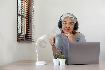 在家戴耳机时使用笔记本电脑的年长妇女     快乐的老年人生活方式和技术概念退休电话桌子商务互联网女士微笑祖母教育会议图片