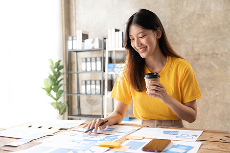 年轻亚洲设计师女性在手机上绘制网站大纲和网页UX应用程序开发图时电脑药片技术工作电话笔记本桌子编程原型团队图片