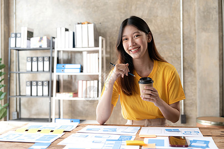 年轻亚洲设计师女性在手机上绘制网站大纲和网页UX应用程序开发图时网络办公室商业桌子项目工作技术电话细胞编程图片