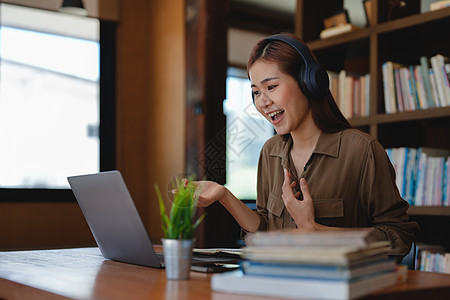 亚洲语言导师开始在线课程 学员挥手微笑着看着电脑屏幕 戴耳机的女性远程交流 电子学习过程 应用程序使用概念学校技术商务工作办公室图片