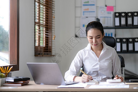 在办公室的笔记本电脑上工作的年轻女子 亚洲女商务人士坐在她办公室的工作场所 美丽的自由职业者女性在她家在线工作员工生意人快乐微笑图片